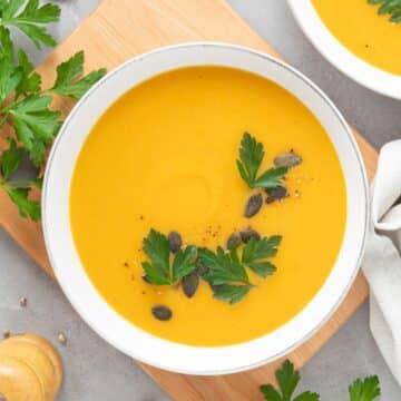 butternut squash soup in a white bowl with parsley and toasted pumpkin seeds