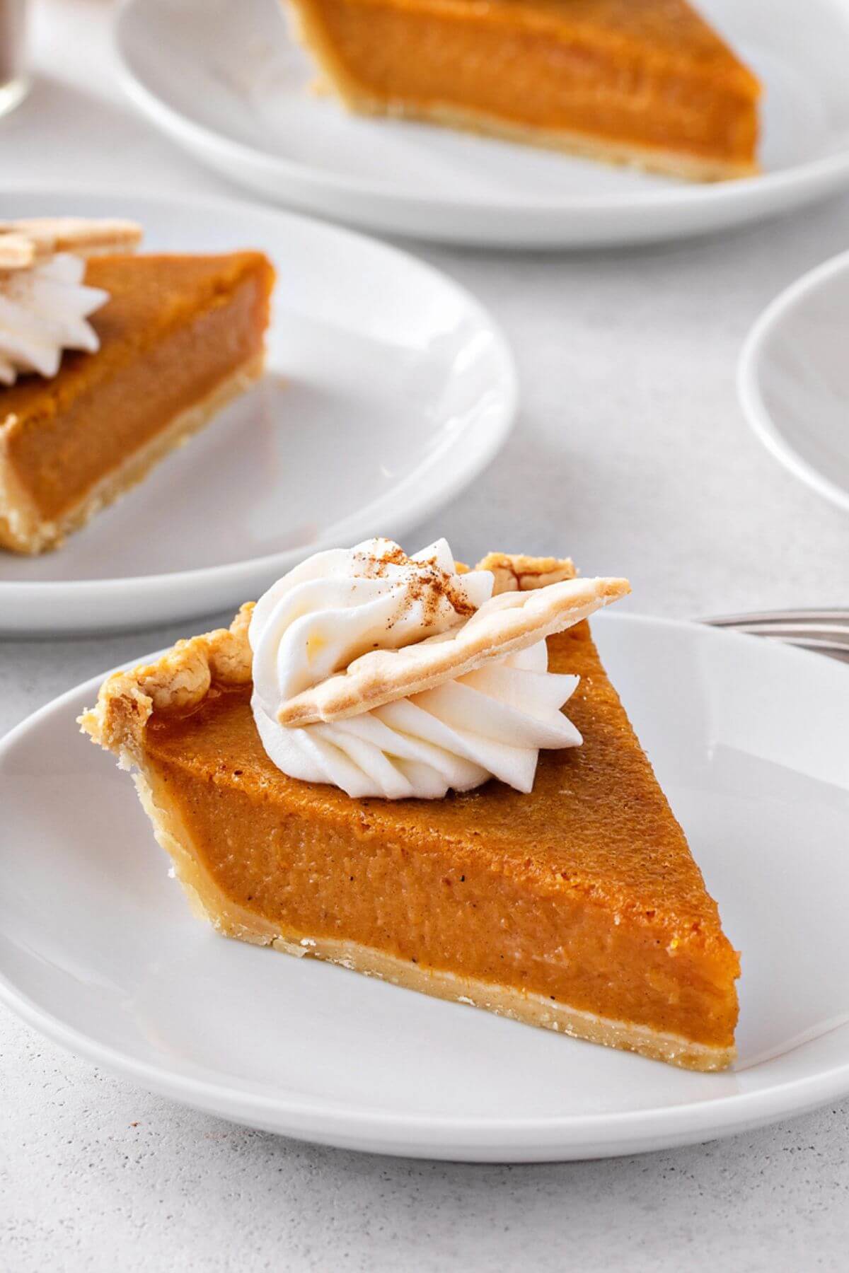 a slice of pumpkin pie with whipped cream on top and leaf decoration