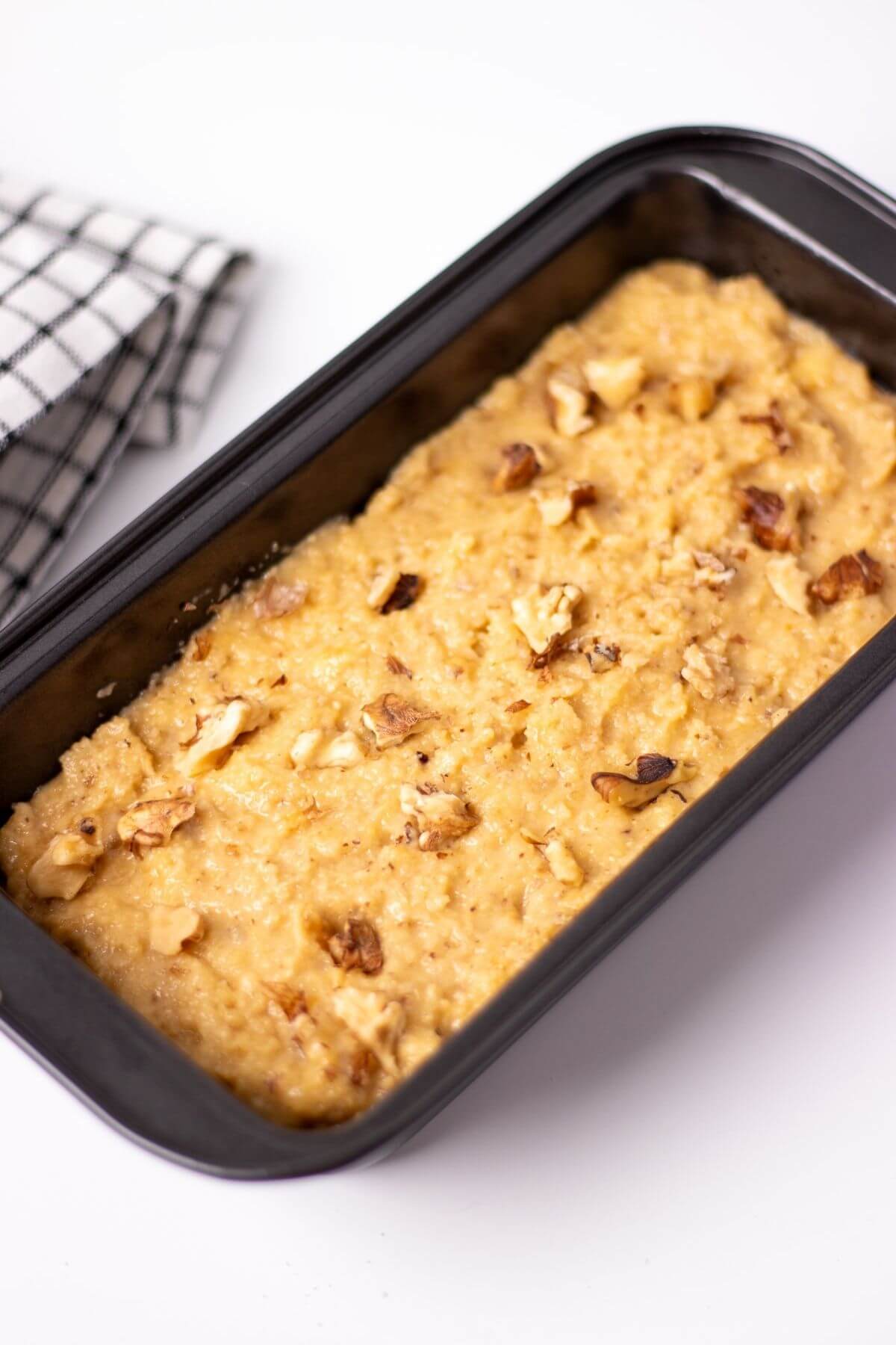 low carb banana bread batter on a loaf pan with pieces of walnuts on top