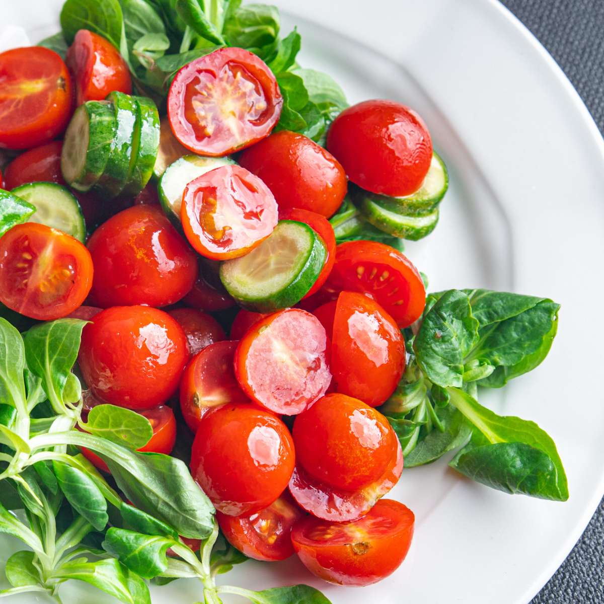 tomato salad - tomatoes, cucumbers, green herbs on white plate