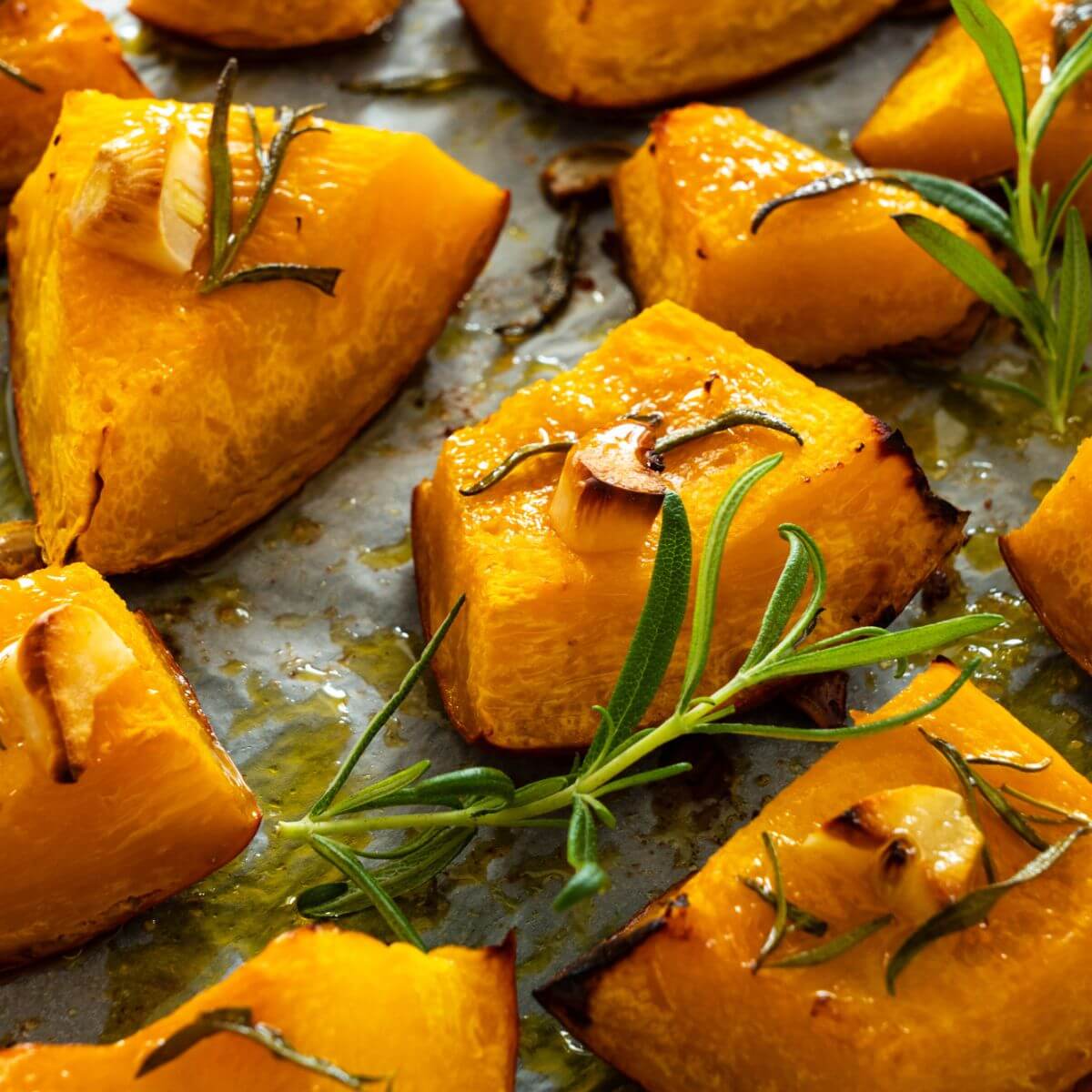 roasted and roughly cubed butternut squash on a sheet pan with herb toppings