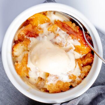 a serving peach cobbler in a ramekin with vanilla ice cream on top