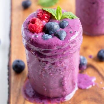 a glass of mixed berry smoothie with fresh berries on top