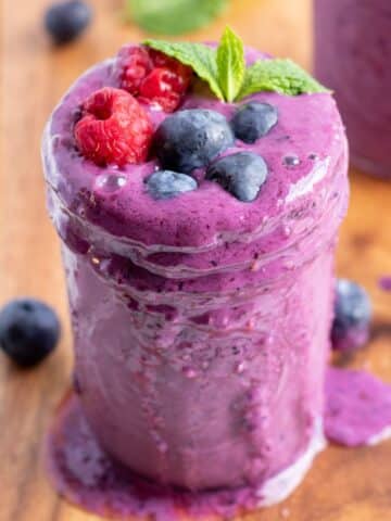 a glass of mixed berry smoothie with fresh berries on top